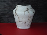a white and black vase on a red surface